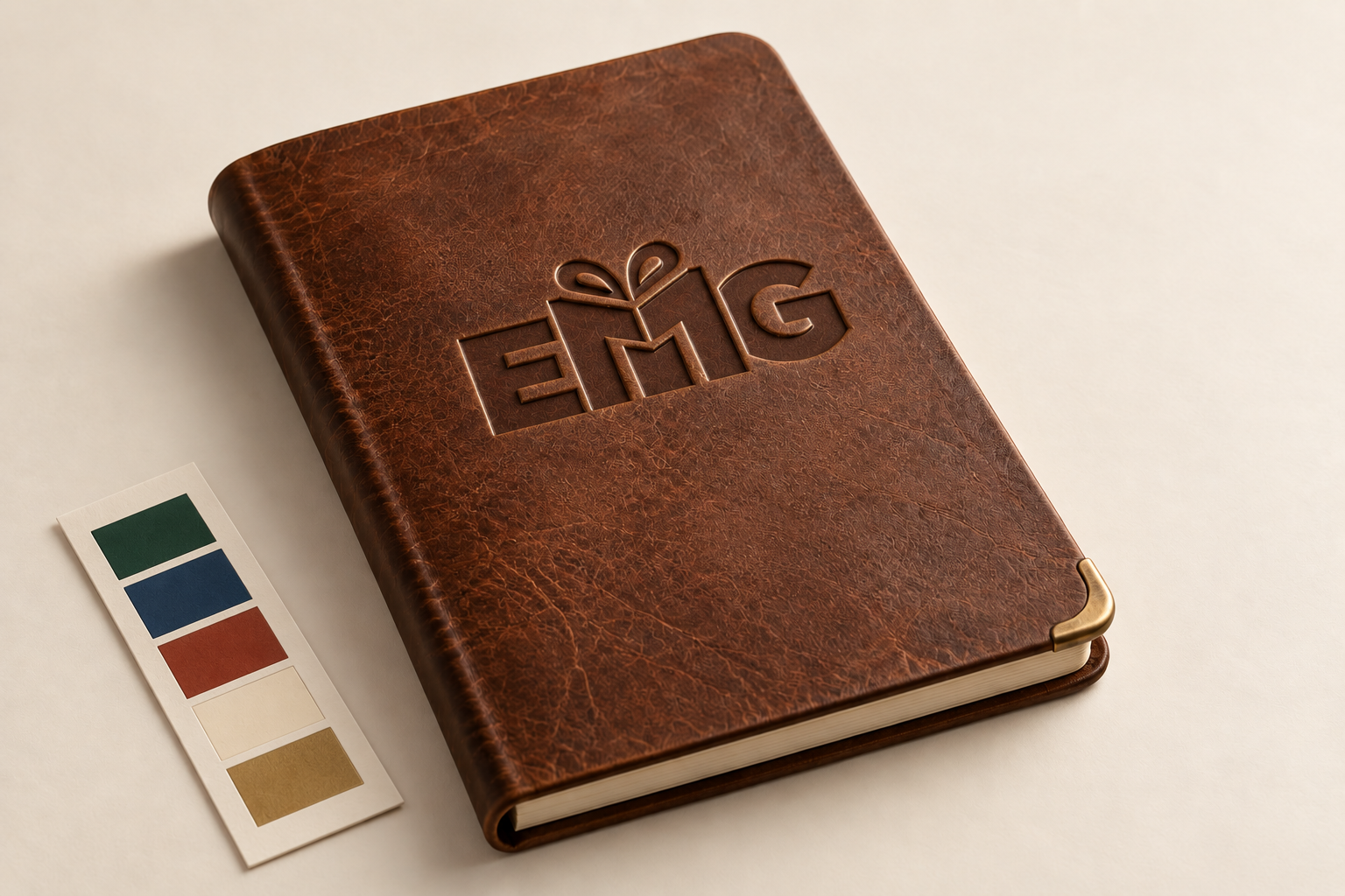 Debossed EMG mark on a leather notebook beside a five-color control strip